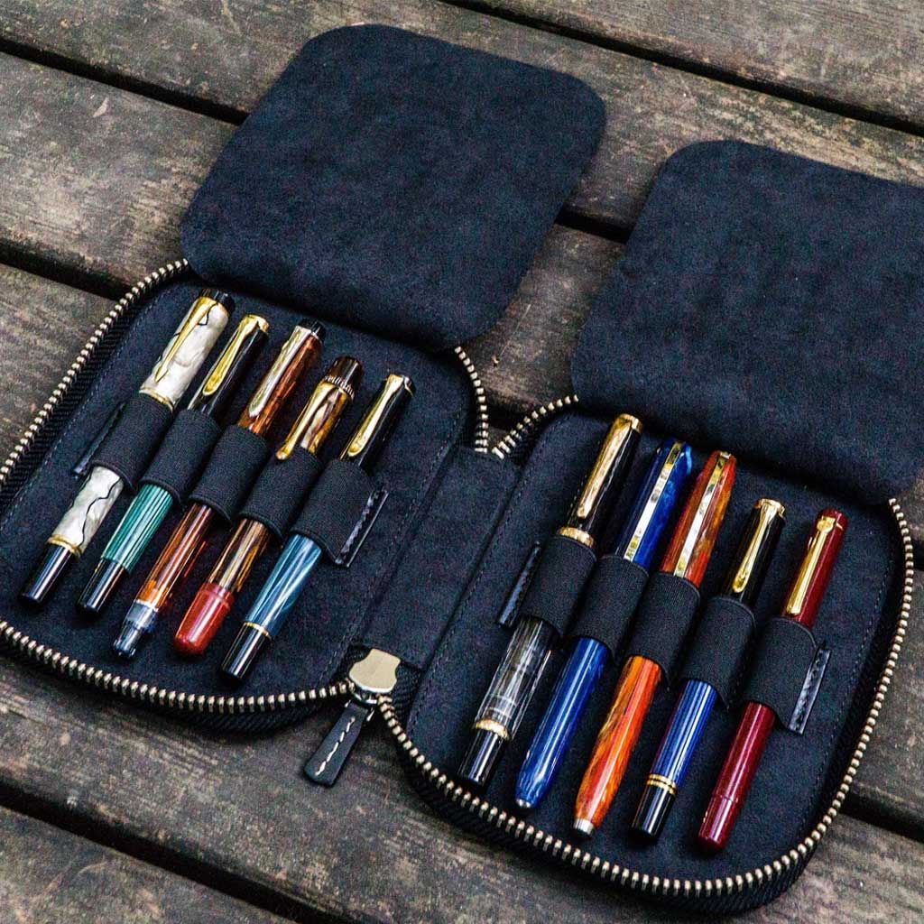 Black leather pen case with ten pens and zipper on a wooden surface