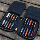 Black leather pen case with ten pens and zipper on a wooden surface