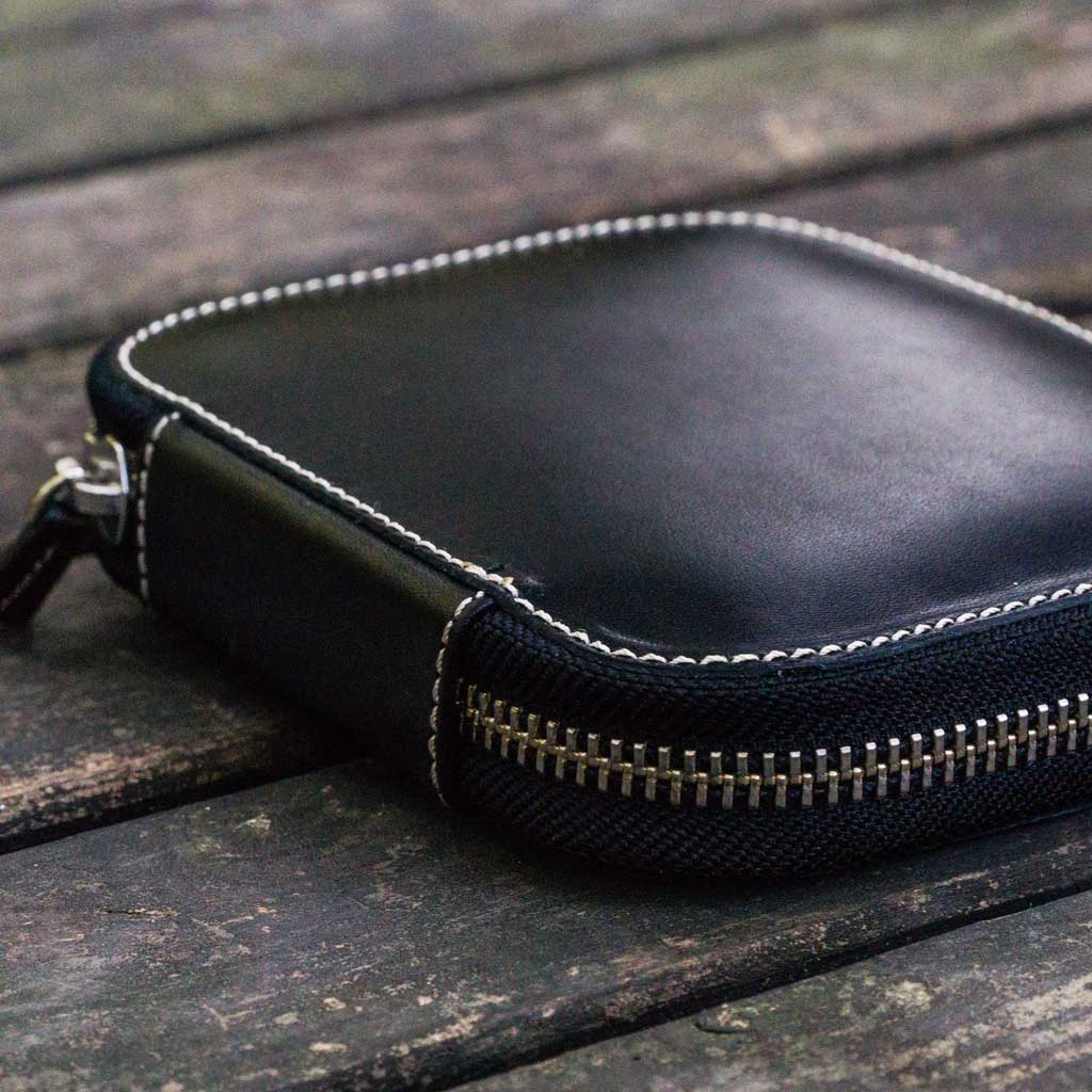 Black leather pen case with zipper on a wooden surface