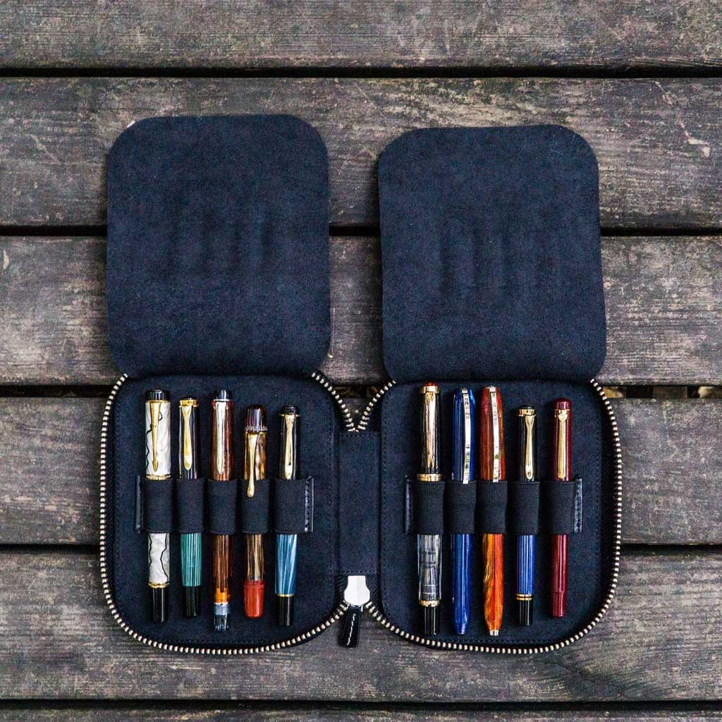 Black leather pen case with zipper  and ten pens on a wooden surface
