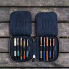 Black leather pen case with zipper  and ten pens on a wooden surface