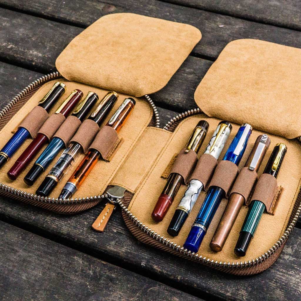 Brown leather pen case with ten pens and zipper on a wooden surface