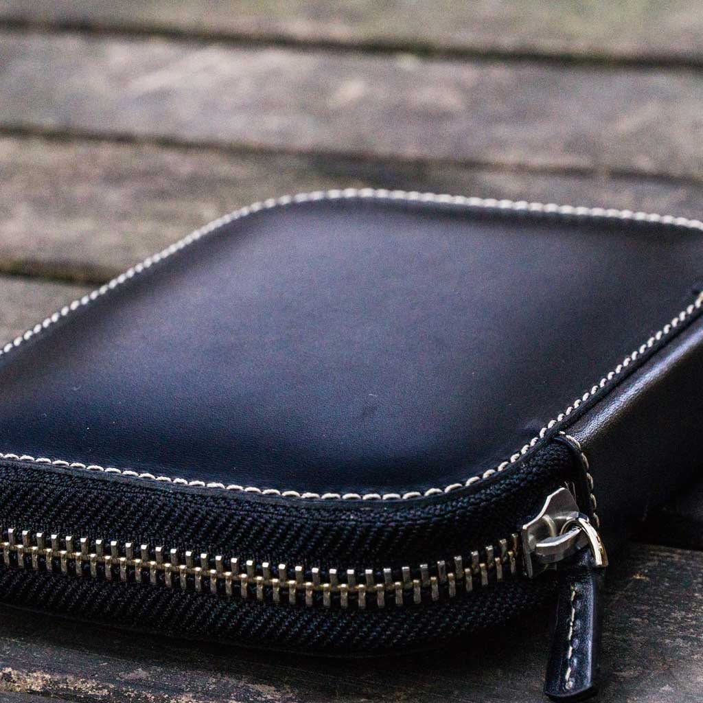 Black leather pen case with zipper on a wooden surface