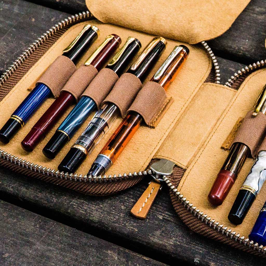 Set of ten fountain pens in a brown zippered pen case on a wooden surface