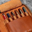 Brown leather zip pen case with writing tools against dark background