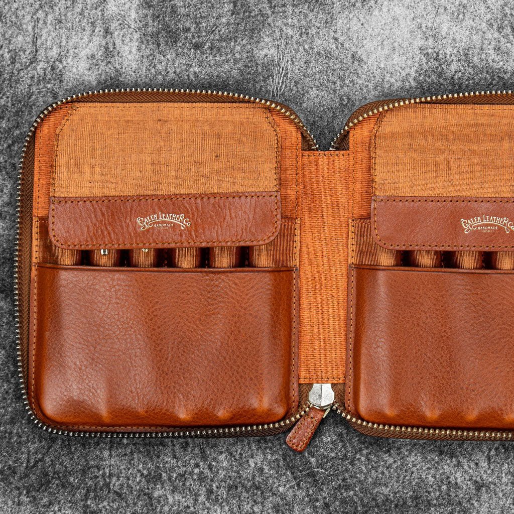 Brown leather zip pen case with writing tools against dark background