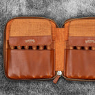 Brown leather zip pen case with writing tools against dark background
