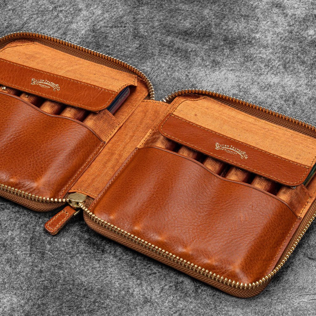 Brown leather zip pen case with writing tools against dark background