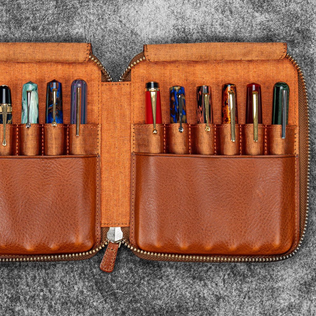 Brown leather zip pen case with writing tools against dark background