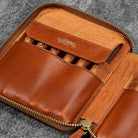 Brown leather zip pen case with writing tools against dark background