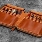 Brown leather zip pen case with writing tools against dark background