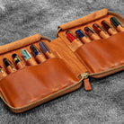 Brown leather zip pen case with writing tools against dark background