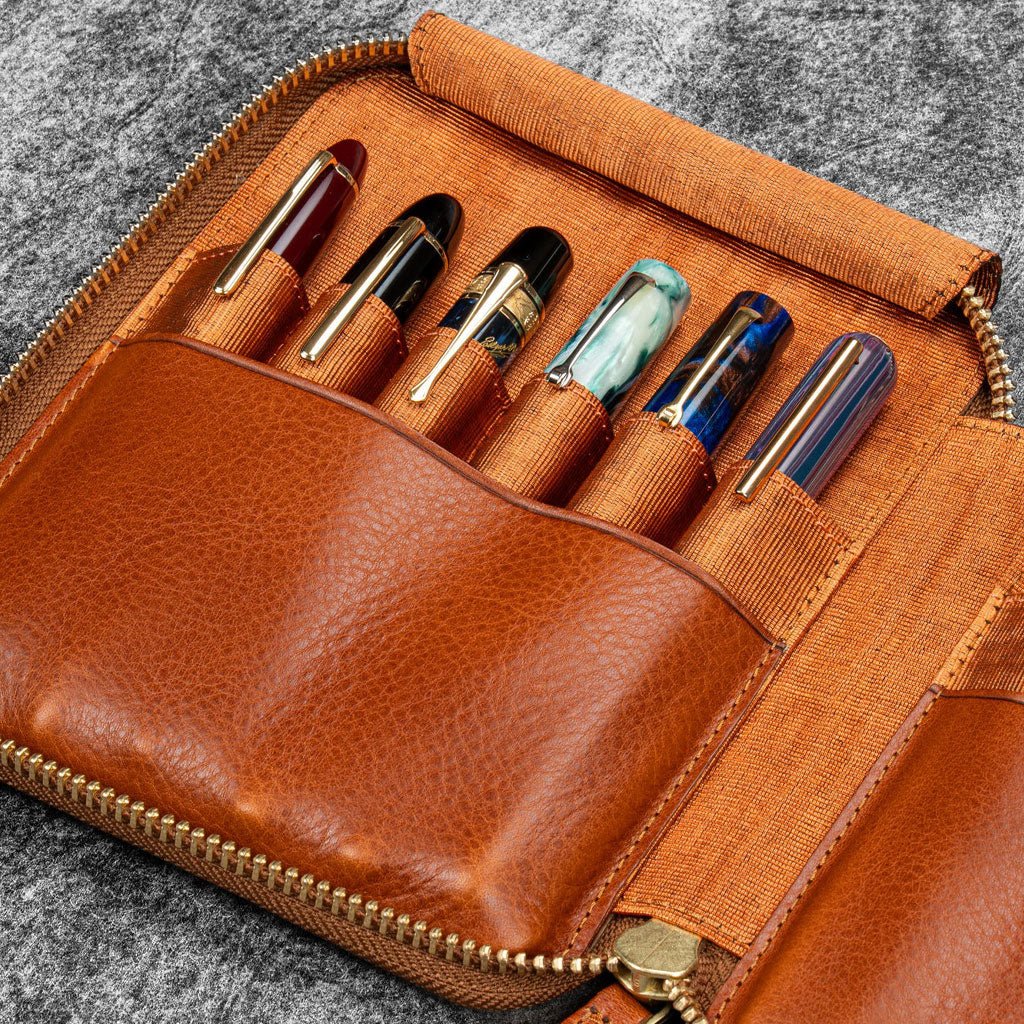Brown leather zip pen case with writing tools against dark background