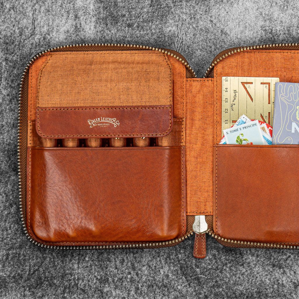 Brown leather zip pen case with writing tools and stationery supplies against dark background