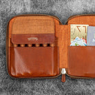 Brown leather zip pen case with writing tools and stationery supplies against dark background