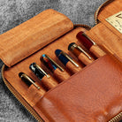 Brown leather zip pen case with writing tools and stationery supplies against dark background