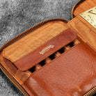 Brown leather zip pen case with writing tools and stationery supplies against dark background