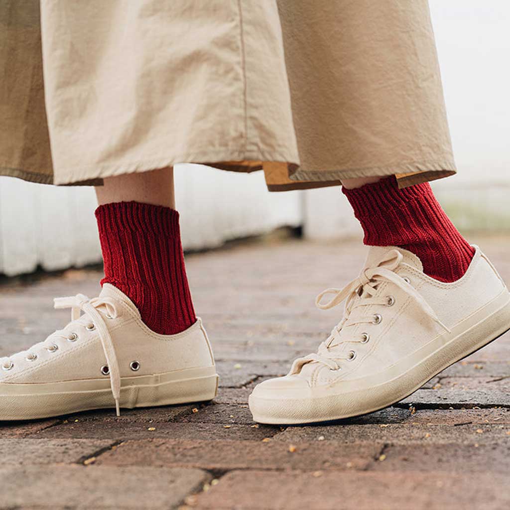 White sneakers with red socks worn on a wooden floor