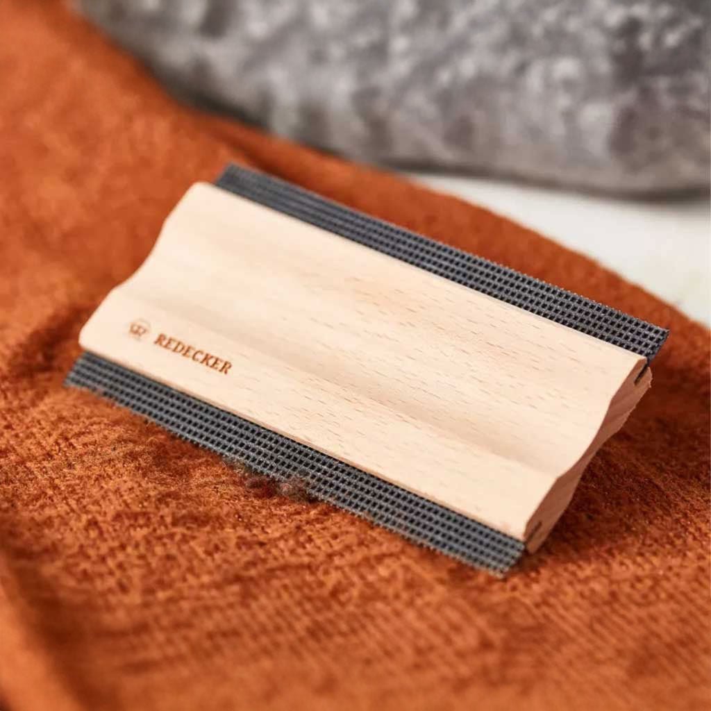 A wooden lint comb on an orange knit fabric.