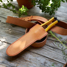 Brown leather tool holster with yellow pliers on a wooden surface with plants in the background