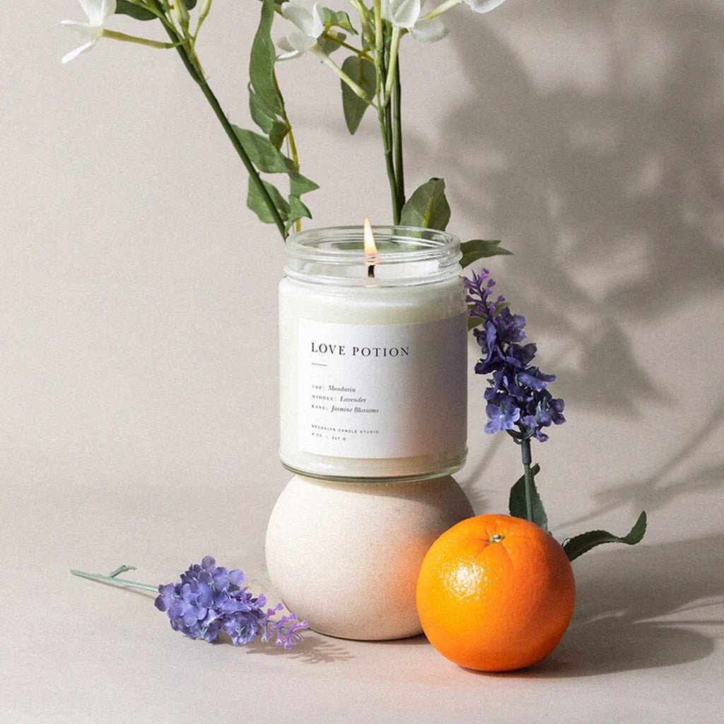 Candle labeled 'Love Potion' with flowers and an orange on a neutral background