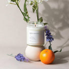 Candle labeled 'Love Potion' with flowers and an orange on a neutral background