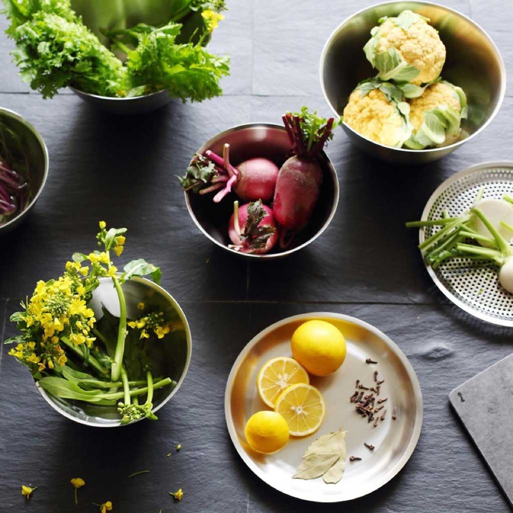 Stainless steel bowls and trays with fresh produce on dark background