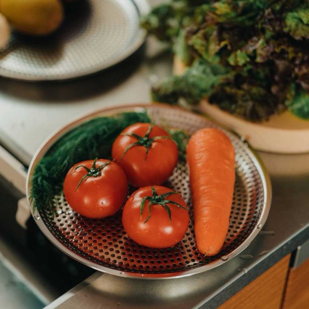 Rinsed vegetables and produce resting on stainless steel strainer in kitchen