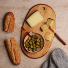 Wooden charcuterie board with cheese, bread and olives on a light background.