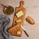 Wooden charcuterie board with cheese, bread and olives on a light background.