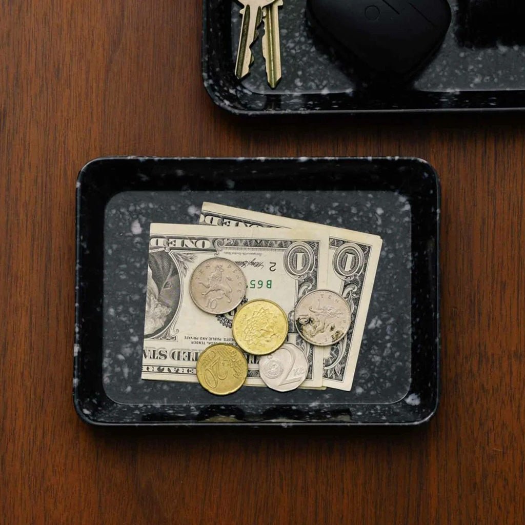 Black marbled tray with dollar bills and coins on a wooden surface