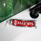 Open Marvis Cinnamon Mint toothpaste tube with toothpaste on bathroom sink.