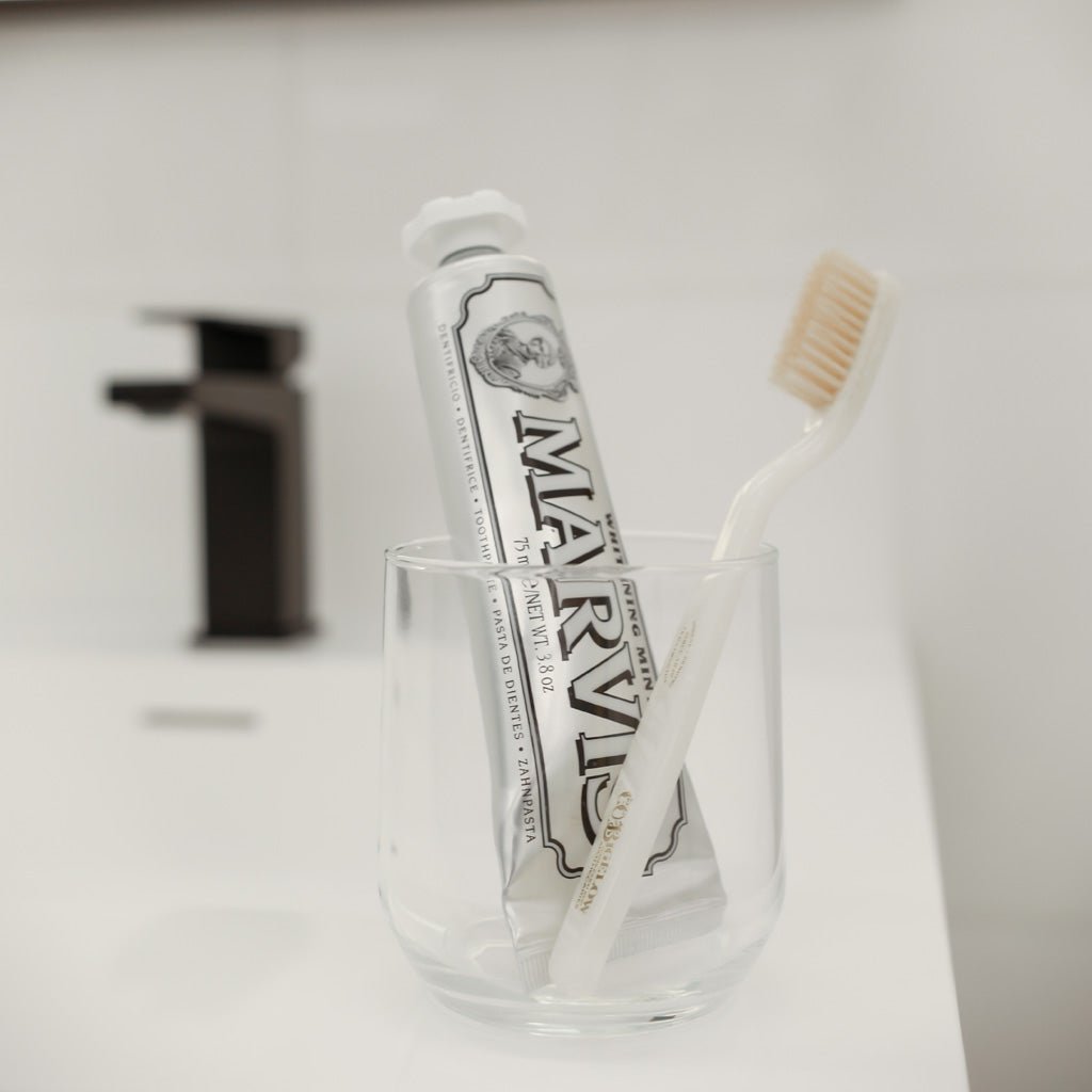 Tube of Whitening Mint Marvis toothpaste in glass next to white toothbrush.
