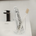 Tube of Whitening Mint Marvis toothpaste in glass next to white toothbrush.