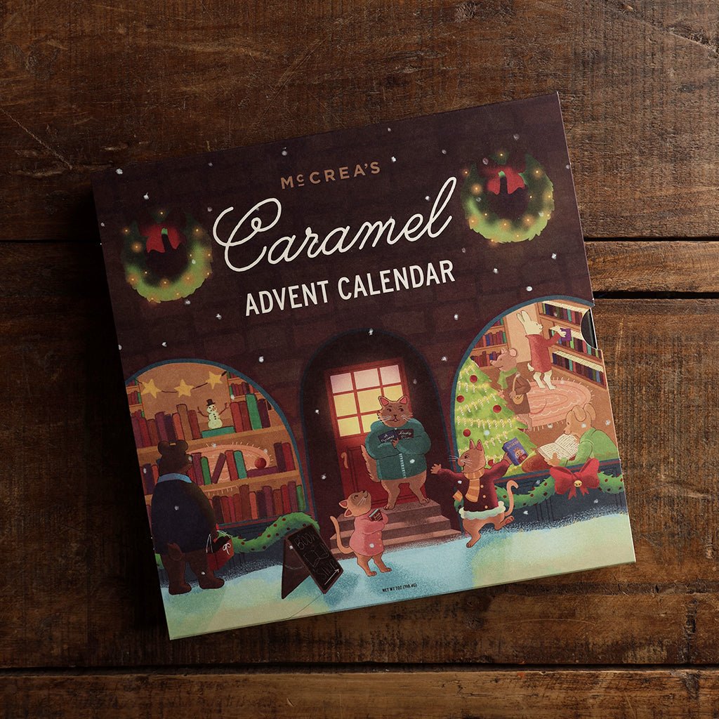 McCrea's Caramel Advent Calendar featuring a cozy holiday-decorated bookshop exterior set on a wooden table. 