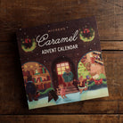 McCrea's Caramel Advent Calendar featuring a cozy holiday-decorated bookshop exterior set on a wooden table. 