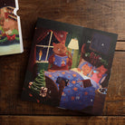 Illustrated advent calendar with numbered doors featuring three cats reading in bed beside a Christmas tree.