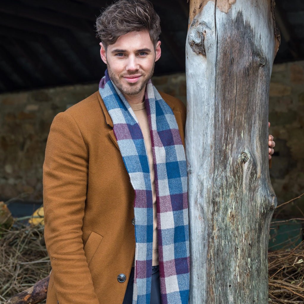 A man wearing a brown coat and checkered scarf next to tree.