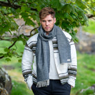 A man wearing a black herringbone wool scarf in front of a natural background.