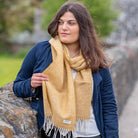 A woman wearing a yellow lambswool scarf in front of a natural background.
