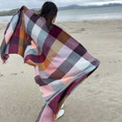 Woman holding checkered wool wrap on beach shore.