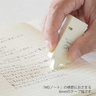 Hand using MD paper correction tape dispenser on page with Japanese text