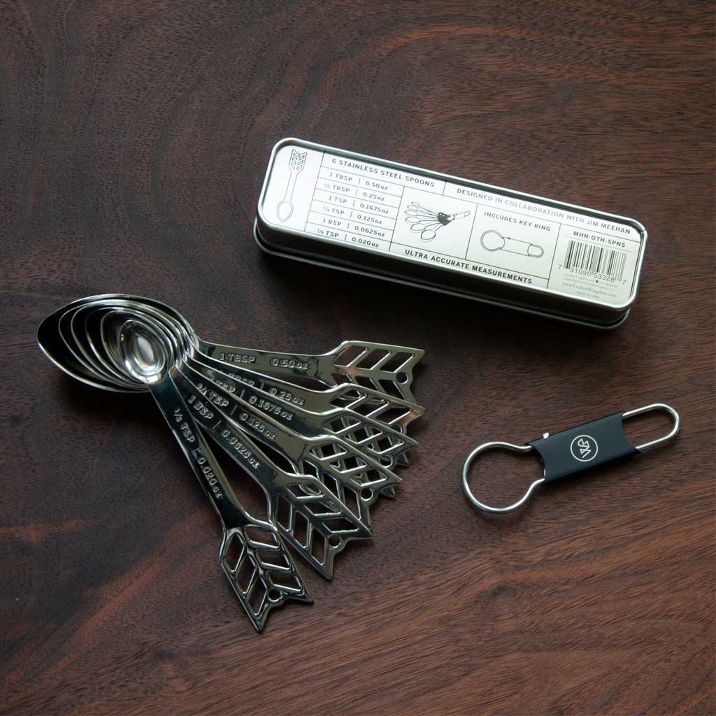 Set of metal measuring spoons with a keychain and packaging on a wooden surface