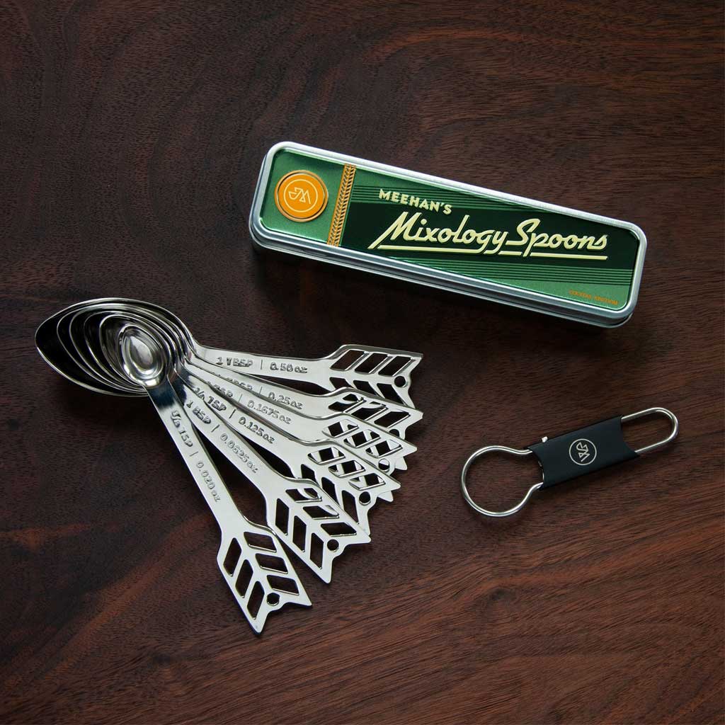 Set of metal measuring spoons with a 'Meehan's Mixology Spoons' tin on a wooden surface.