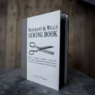 Sewing book titled 'Merchant & Mills Sewing Book' with a pair of scissors illustration in front of a wooden background.