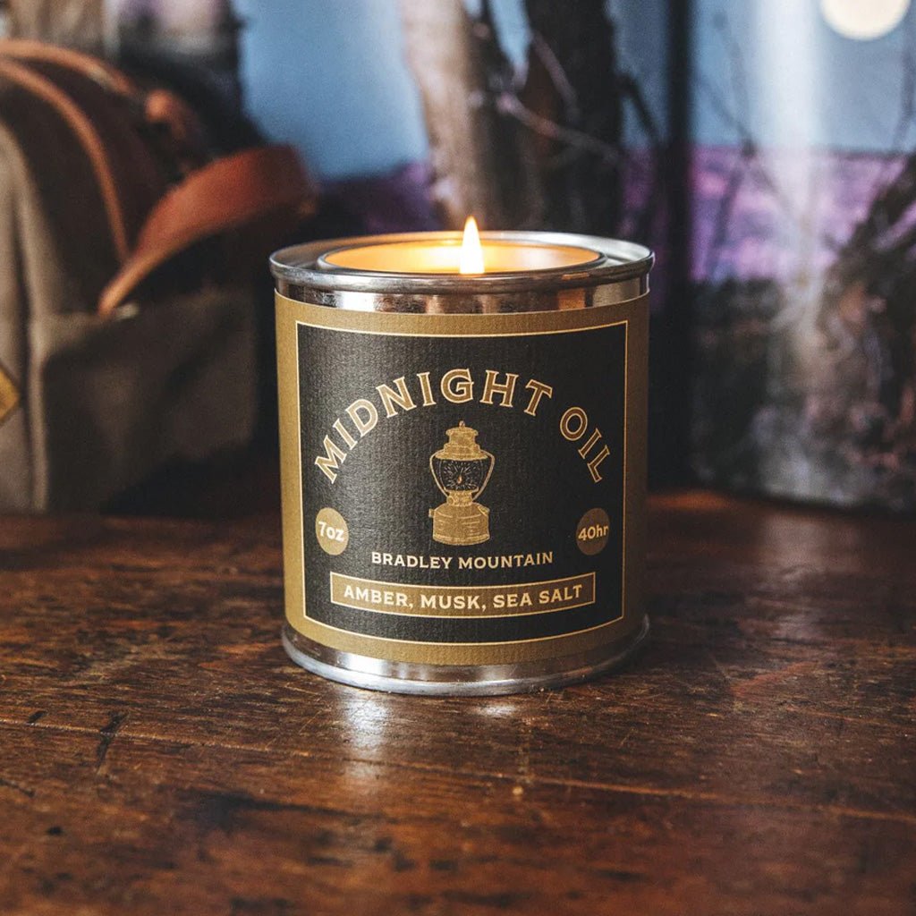 Candle in a can labeled 'Midnight Oil' on a wooden surface