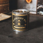 Candle canister labeled 'Midnight Oil' by Bradley Mountain on a dark surface.
