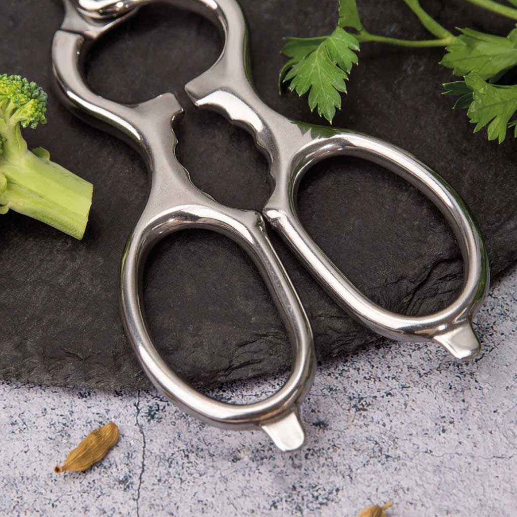 Metal kitchen shears on a dark stone surface with vegetables.