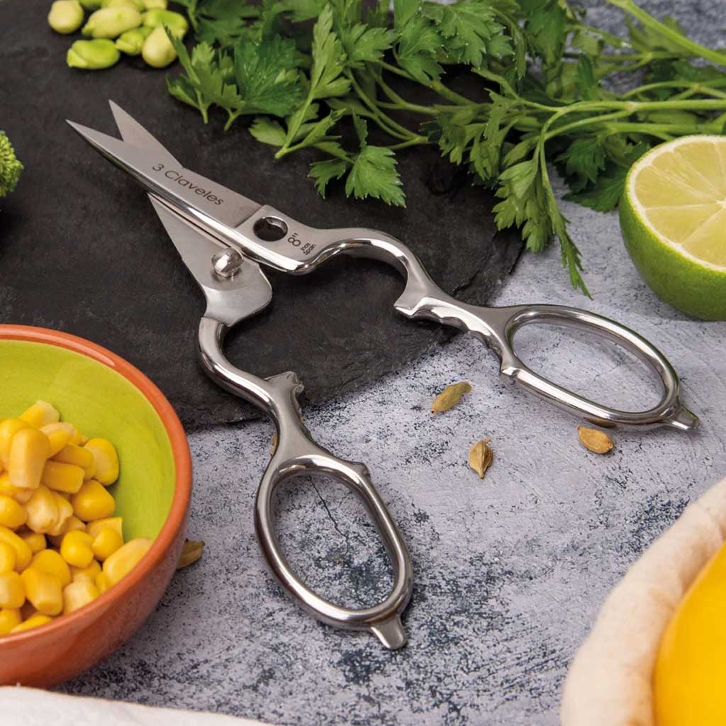 Pair of kitchen shears on a surface with vegetables and a lime.