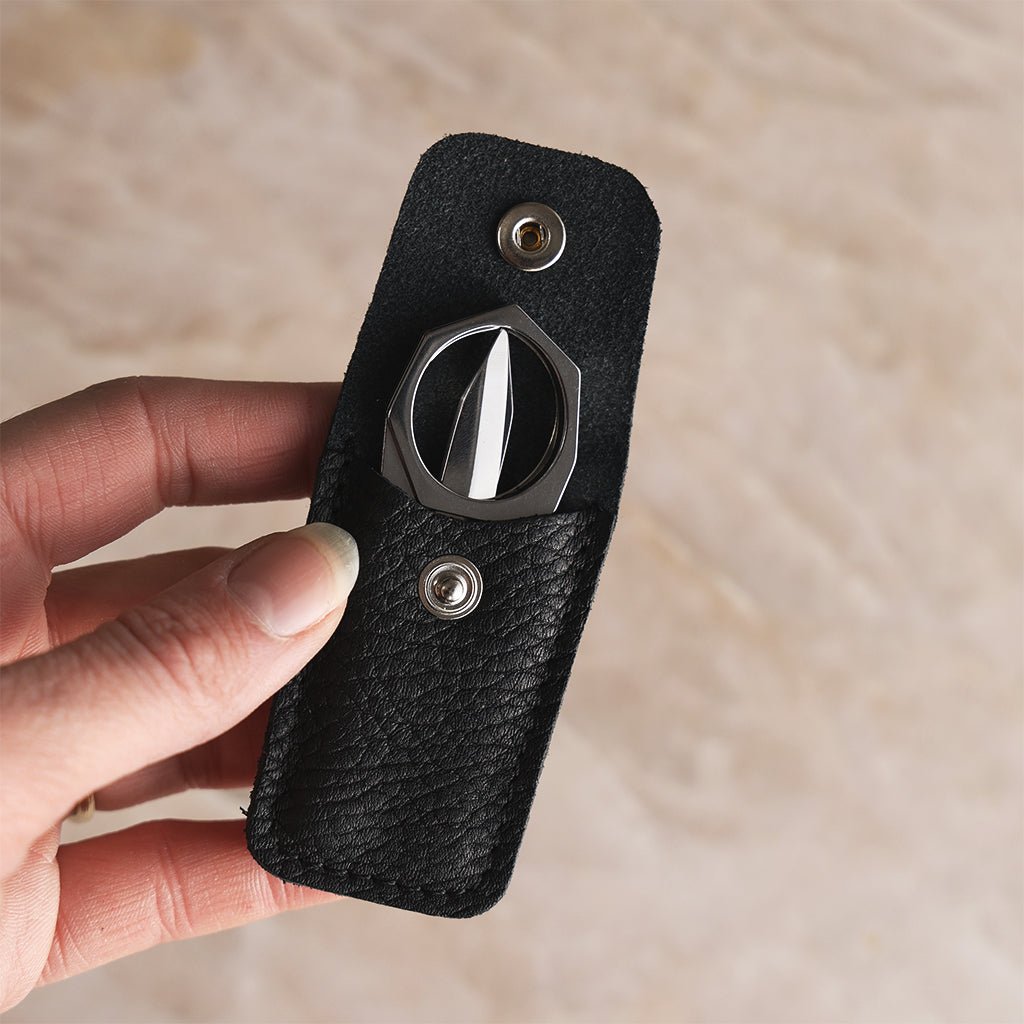 Hand holding an open black leather case with Nogent foldable scissors tucked inside, showing their compact size.